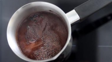 Aromatik kahve Türk 'te kaynıyor ve köpükler ağzına kadar doluyor. Sabah kahvaltısı ya da kahve molası için bir içki. Bir kafede ya da mutfakta sıcak bir içecek hazırlamanın geleneksel yolu. Yavaş çekim.