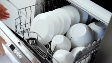 A young woman closes the dishwasher with white dishes. Build into the kitchen. Modern home kitchen. Housework.