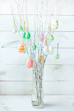 The branches of the trees decorated with multi-colored Easter eggs stand in a vase on a white wooden background. Easter tree. Easter composition.