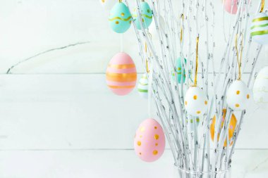 The branches of the trees decorated with multi-colored Easter eggs stand in a vase on a white wooden background. Easter tree. Easter composition.