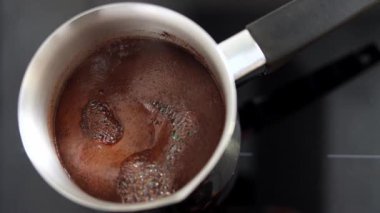 Aromatik kahve Türk 'te kaynıyor ve köpükler ağzına kadar doluyor. Sabah kahvaltısı ya da kahve molası için bir içki. Bir kafede ya da mutfakta sıcak bir içecek hazırlamanın geleneksel yolu. Yavaş çekim.