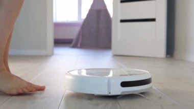 Close up a young girl is approaching the robot vacuum cleaner and pressing the start button. Automatic electric cleaning inside the apartment. Robotic cleaner technology. Modern technologies in-house