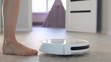 Genç bir kız elektrikli süpürgeye yaklaşıyor ve yavaş çekimde başlatma düğmesine basıyor. Dairenin içinde otomatik elektrikli temizlik. Robot temizleme teknolojisi. Modern
