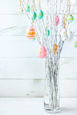 The branches of the trees decorated with multi-colored Easter eggs stand in a vase on a white wooden background. Easter tree. Easter composition.