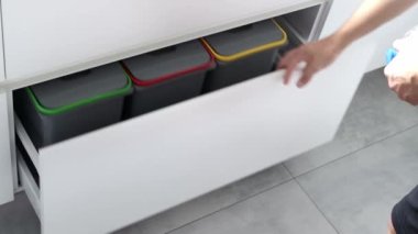 Genç bir adam mutfaktaki konteynırlarda çöpleri ayırıyor. Atık ayıklama sistemi olan modern bir mutfak. Atık Ayrım Konsepti. Sıfır kayıp. Çevre dostu. 4K görüntü.