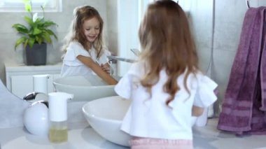 Tuvaletteki kız. 4-5 yaşlarında küçük bir kız büyük bir aynanın önünde tek başına ellerini yıkıyor. Çocuk hijyeni. 4k görüntü.
