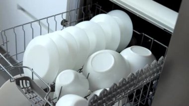 A young woman closes the dishwasher with white dishes. Build into the kitchen. Modern home kitchen. Housework.
