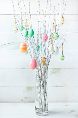 The branches of the trees decorated with multi-colored Easter eggs stand in a vase on a white wooden background. Easter tree. Easter composition.