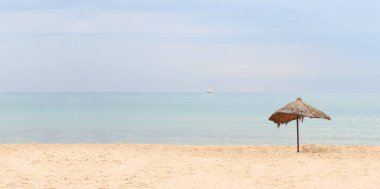 Deniz manzarasının bayrağı. Güneşli bir günde mavi denizin arka planında tropik bir kumlu sahilde saman plajı şemsiyesi. Idyllic seyahat ve yaz tatili konsepti.