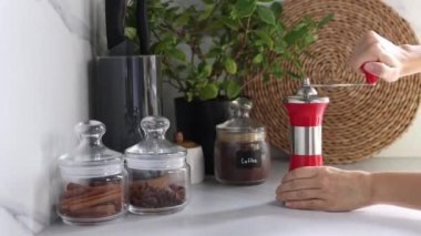 Kadın elleri, modern bir mutfağın arka planında kahve çekirdeklerini öğütüyor. Kendi kahveni öğütüyorsun..