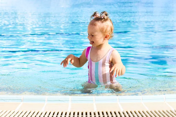 stock image A funny little girl of European appearance in a swimming pool on a hot sunny day. Concept of a happy childhood. The concept of tourism and recreation. Advertisement of a hotel or a vacation tour.