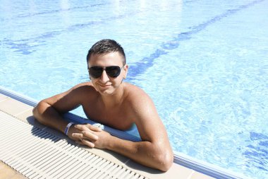 Avrupalı görünümlü genç bir adam havuzda gülümsüyor. Turizm, tatil ve dinlenme konsepti. Otel kompleksinin reklamı..