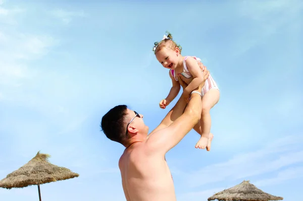 stock image A young dad holds his tiny daughter above him against the sky on the beach. Concept of a happy childhood, parenthood, and happy family. The concept of tourism and recreation.