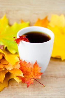White cup of tea and autumn maple leaves on wooden background. The concept of calm, relaxation and autumn. Autumn vertical background.