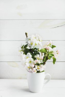 Beyaz ahşap arka planda beyaz çiçekli güzel bir elma ağacı filizi. Suyla dolu bir bardakta çiçek açan dal. Bahar hala hayattır. Mesaj için yer. Bahar ya da Anneler Günü kavramı.