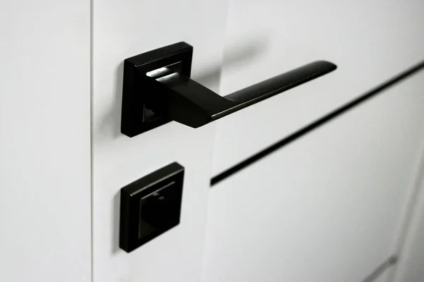 Close-up of the stylish new metal door knob on a modern white interior door. Concept of interior details. Joinery. Door lock. Door fittings. Modern interior in the style of minimalism.