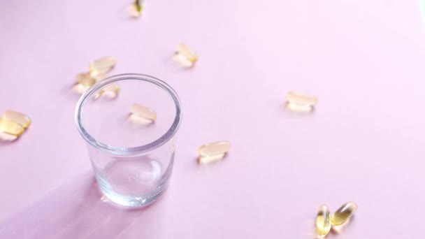 透明的 含有维生素的黄色胶囊被倒入一个透明的杯子中 杯子的背景是粉红色的 鱼油补充剂健康 维生素和医药的概念 Omega 维生素D 4K镜头 — 图库视频影像