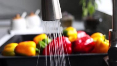 Yellow and red pepper are washed in a special tray for vegetables. The stream of water pours on the pepper in the sink. Slow motion. The interior of a modern kitchen.