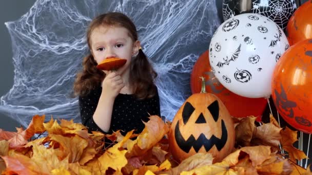 Ein Kleines Hexenmädchen Verspeist Auf Dem Hintergrund Von Halloween Attributen — Stockvideo