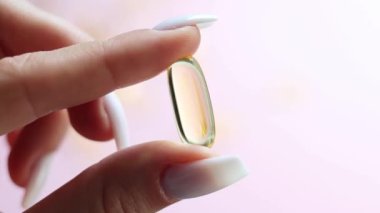 Genç kadın elleri sarı omega-3 jel kapsülünü yakından tutuyor. Balık yağı takviyesi. Sağlık, vitamin ve ilaç kavramı. Omega 3 balık yağı kapsülleri, E vitamini. Yavaş çekim..