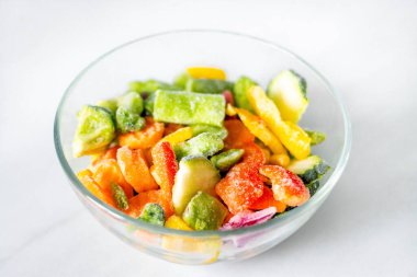 Beyaz arka planda cam tabakta donmuş sebzeler. Sağlıklı beslenme kavramı.