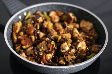 Şef tavada pişirilmiş etli sebzelerin üzerine sos döker. Bir restoranın mutfağında yemek pişirmek..