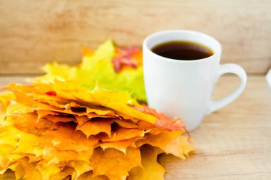 White cup of tea and autumn maple leaves on wooden background. The concept of calm, relaxation and autumn. Autumn background.