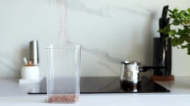 Karabuğday tarlaları modern bir mutfağın arka planına karşı şeffaf bir kabın içine dökülür. Sağlıklı gıda ve beslenme konsepti. Güvenli, ekolojik ve sağlıklı ürünler. Ekolojik Paketleme