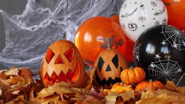 Lantern carved from pumpkin known as Jack-o-lantern on a black background with spider webs, autumn leaves and balloons. Halloweens holiday attributes. Trick or treat.