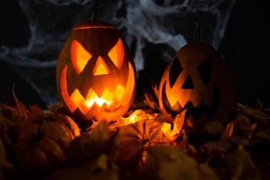 Halloween's holiday attributes. Lantern carved from pumpkin known as Jack-o-lantern glow in the dark on a black background with spider webs, autumn leaves and balloons. Trick or treat.