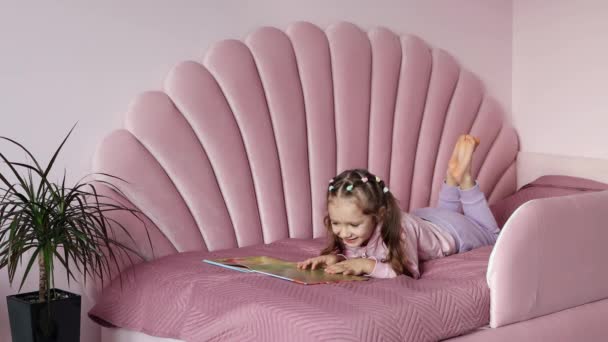 Ένα Κοριτσάκι Είναι Ξαπλωμένο Στο Κρεβάτι Κοιτάζοντας Βιβλίο Επιλέξετε Ένα — Αρχείο Βίντεο