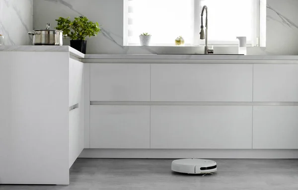 The automated robot vacuum cleaner is cleaning the floor in the kitchen in slow motion. Automatic electric cleaning inside the apartment. Robotic cleaner technology. Modern technologies in-house. Home cleaning.