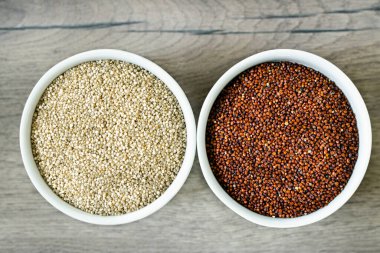 Ahşap arka plandaki iki beyaz tabakta kırmızı ve beyaz kinoa. Sağlıklı gıda ve beslenme konsepti. Güvenli, ekolojik ve sağlıklı ürünler.