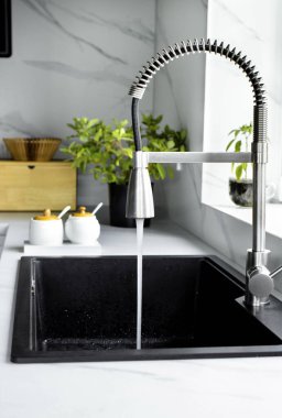 Mutfak musluğundan lavaboya temiz su akıntısı akıyor. Çevre, su kirliliği ve su sıkıntısı kavramı. Ev suyunu fazla kullanıyorsun. Dikey fotoğraf.