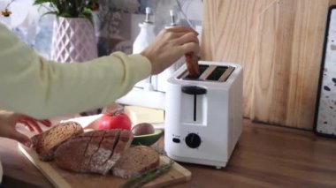 Genç bir kadın ekmek dilimlerini tost makinesine sokuyor. Kahvaltı konsepti. 4k görüntü.