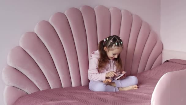 Ένα Κοριτσάκι Ευρωπαϊκής Εμφάνισης Κάθεται Στο Κρεβάτι Και Χρησιμοποιεί Ένα — Αρχείο Βίντεο