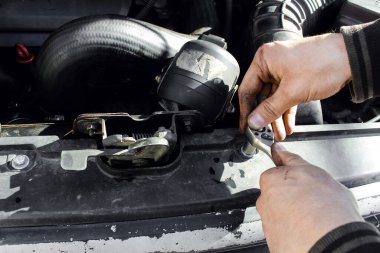 The mechanic twists the radiator grill with a key close up. Disassembled car. Car engine room under maintenance. Car service station. Car repair. clipart