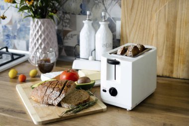 Ekmek kızartma makinesinden çıtır çıtır çavdar ekmeği. Kahvaltıda tost. Modern bir mutfak arka planına karşı tahta bir tahtanın üzerinde duran dilimlenmiş siyah ekmek..