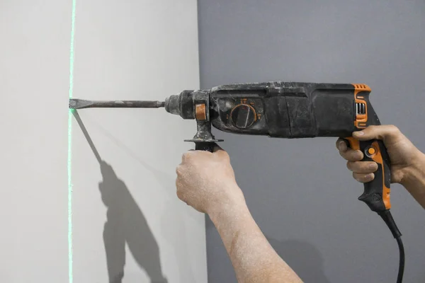 Close-up of a workers hands holding a puncher. A young man drills holes in the wall with a hammer drill. The master works with a hammer drill. Renovation concept.