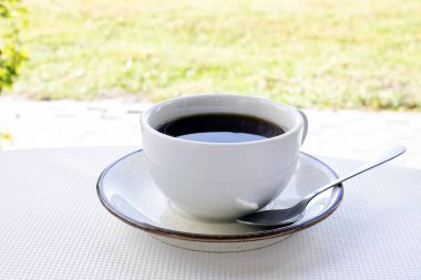 Beyaz bir fincan yakın plan kahve masanın üzerinde nehrin arka planına karşı. Doğada çay partisi. Günaydın..