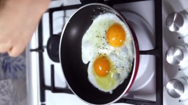 Genç kadın elleri tavada kızaran yumurtaların üzerine öğütücüden biber serpiyor. Kahvaltı konsepti. Dikey görüntüler.