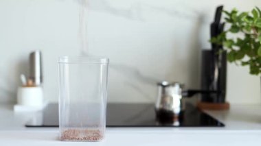 Karabuğday tarlaları, modern bir mutfağın arka planına karşı şeffaf bir kaba yavaş çekimde dökülür. Sağlıklı gıda ve beslenme konsepti. Güvenli, ekolojik ve sağlıklı ürünler. Ekolojik ambalaj, haşere kontrolü.
