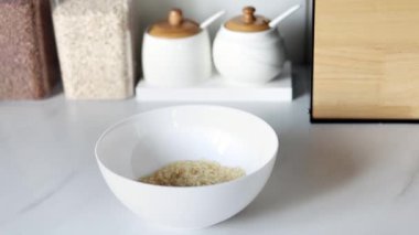 Beyaz çiğ pirinç, modern bir mutfağın arka planına karşı ağır çekimde beyaz bir tabağa dökülür. Sağlıklı gıda ve beslenme konsepti. Güvenli, ekolojik ve sağlıklı ürünler.