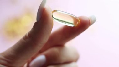 Genç kadın elleri sarı omega-3 jel kapsülünü yakından tutuyor. Balık yağı takviyesi. Sağlık, vitamin ve ilaç kavramı. Omega 3 balık yağı kapsülleri, D vitamini. Yavaş çekim..