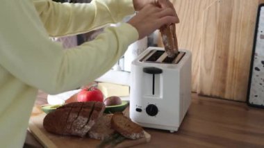 Genç bir kadın ekmek dilimlerini tost makinesine sokuyor. Kahvaltı konsepti. 4k görüntü.