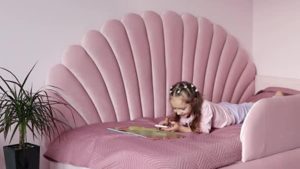 Ένα Κοριτσάκι Είναι Ξαπλωμένο Στο Κρεβάτι Κοντά Στο Βιβλίο Και — Αρχείο Βίντεο