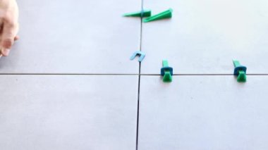 The tiler seramik fayans düzenleme sisteminin takozlarını yavaş çekimde yere düşürüyor. Fayans harcı ayarlanırken plastik klipsli ve takozlu döşeme sistemi.