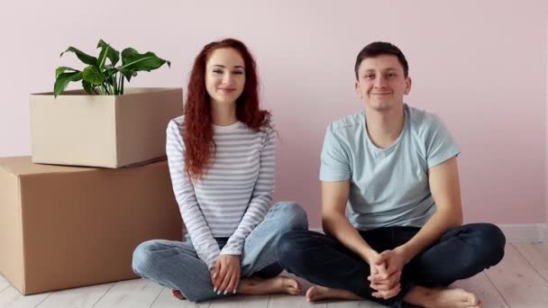 Szczęśliwa Młoda Para Siedzi Podłodze Pobliżu Kartonowych Pudełek Patrzy Kamerę — Wideo stockowe