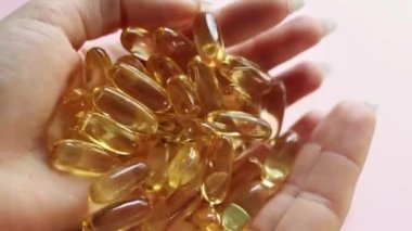 Kapalı kapaklı sarı şeffaf haplar, omega 3 balık yağı kapsülleri, D vitamini. Genç bir kadın elden ele sarı şeffaf kapsüller döker. Sağlık, vitamin ve ilaç kavramı. 4K