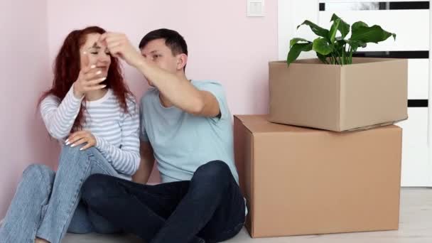 Szczęśliwa Młoda Para Siedzi Podłodze Pobliżu Kartonowych Pudełek Mąż Pokazuje — Wideo stockowe